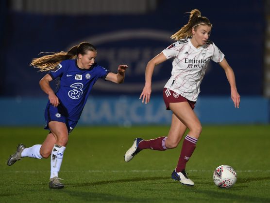Leah Williamson dribbles the ball whilst being chased by Fran Kirby in a match against Chelsea