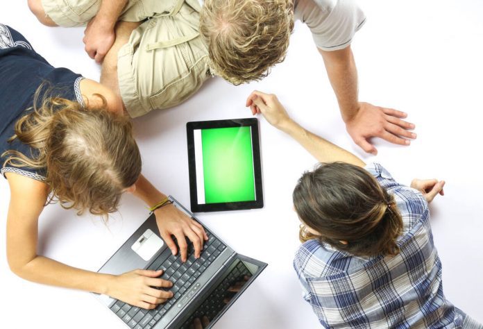 A group of young students using a laptop and an electronic tablet