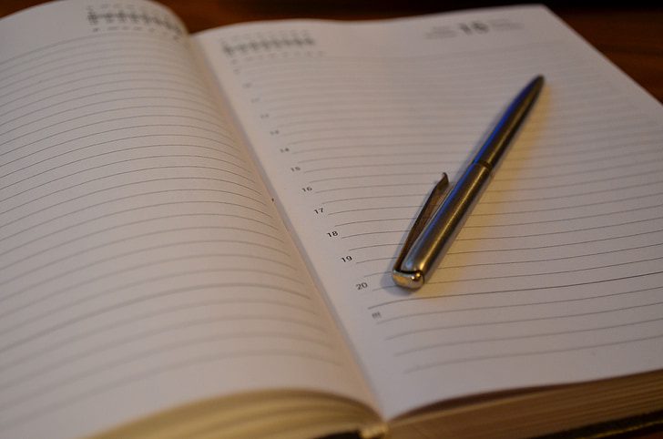 A silver pen sits on a diary with with white pages.