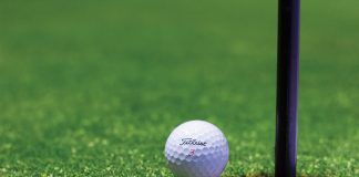 White branded golf ball sits on the left edge of a golf hole with a black pole rising from the ground