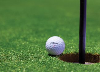 White branded golf ball sits on the left edge of a golf hole with a black pole rising from the ground