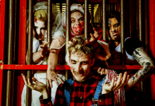 This is a photo of four scare actors in full makeup and costume. Three of them are trapped behind bars reaching towards the fourth.