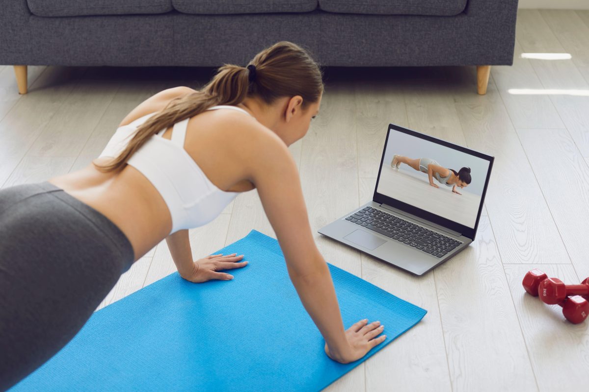 A photo of a girl doing pilates at home with a laptop video up.