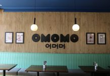 A photo of one of the wall inside the restaurant, with wooden background and black big OMOMO logo on it.