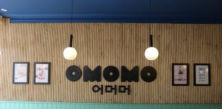 A photo of one of the wall inside the restaurant, with wooden background and black big OMOMO logo on it.