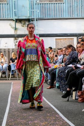 A model walking down the runway in a very colourful outfit wearing a skirt and a coat walking down the runway.