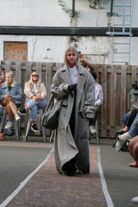 A model walking down the runway wearing a long grey coat and a bag in the same colour.