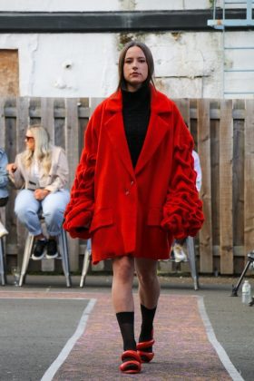 A model walking down the runway wearing an oversized red coat.