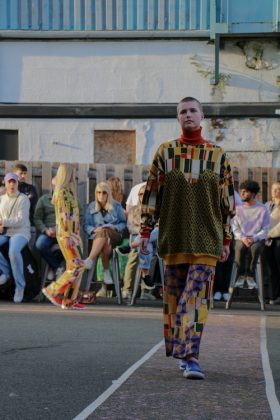 A model walking down the runway in one of the colourful outfits and many people watching her.