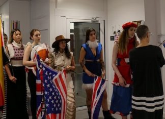 Models in outfits from first-year students being shown how to wave a flag and walk.