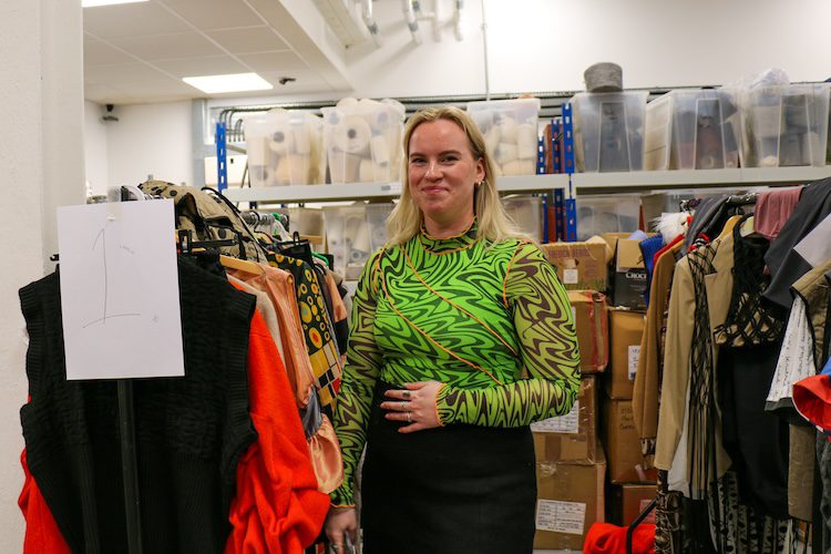 Fashion student Sarah Zechner standing beside a rack with outifts from her collection.