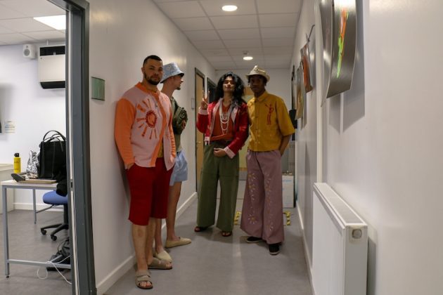 Male models in colourful outfits posing in the backstage after walking down the runway.