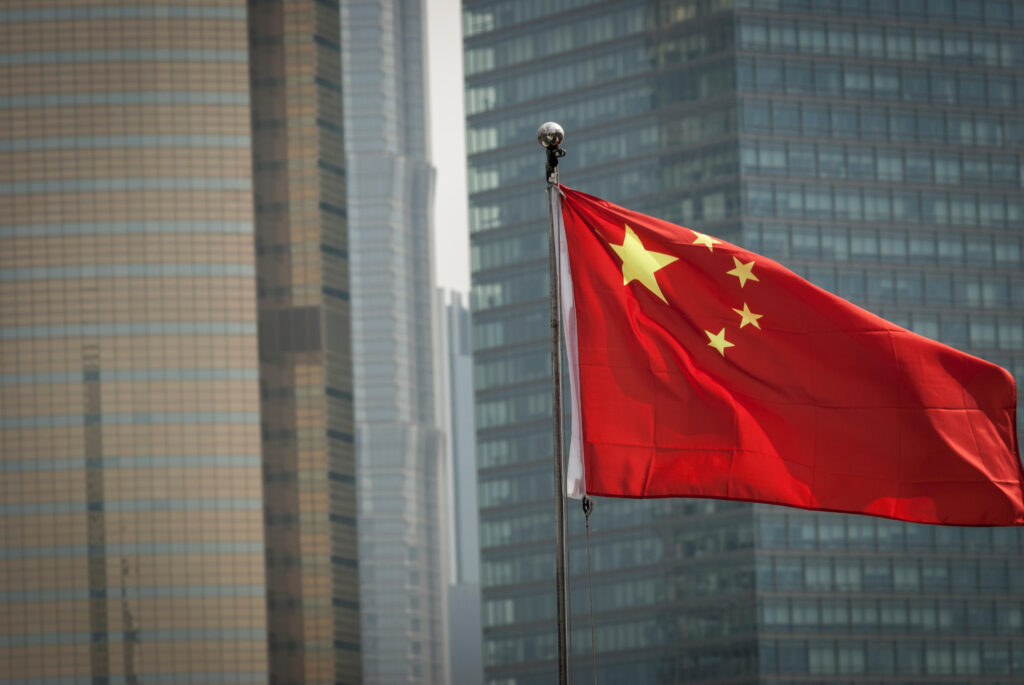 Chinese flag (red with five gold stars) in Shanghai with modern buildings in the background.