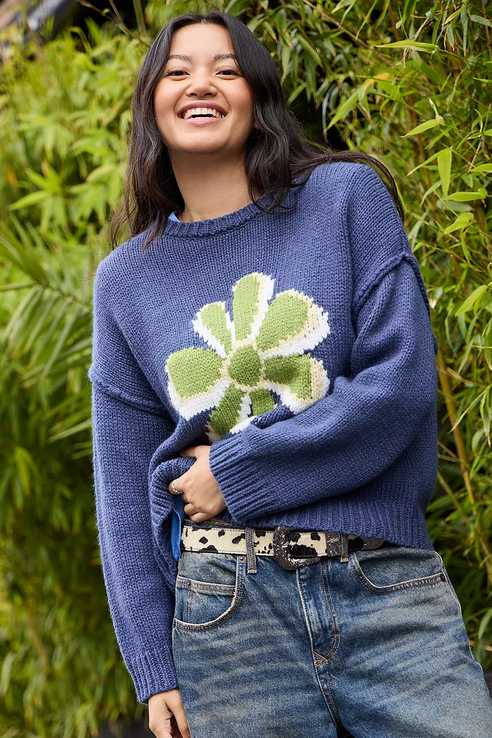 Person wearing a cobalt blue sweater with a large green flower design, paired with denim jeans.