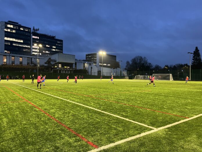 Derby men's seconds face Nottingham Trent men's seconds at Kedleston Road. Derby are in orange, with Trent in pink under the floodlights.