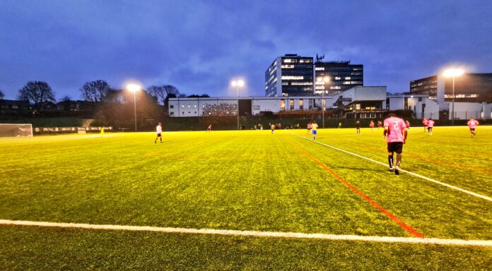 Derby men's seconds face Nottingham Trent men's seconds at Kedleston Road. Derby are in orange, with Trent in pink under the floodlights.