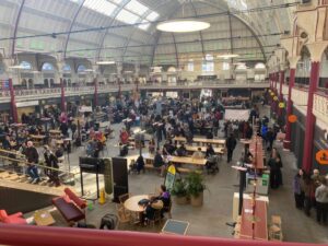 This image shows a crowd of people visiting the Derby farmers market at the Derby Market Hall from the corner of the balcony.