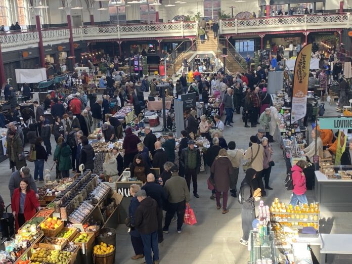 This image shows a crowd of people inside Derby Market Hall visiting the Farmers Market.