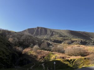 The image contains a picture of Mam Tor from a distance.
